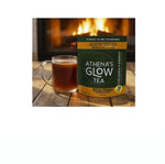 Athena's Glow Tea package with a mug of tea on a wooden surface in front of a fireplace.