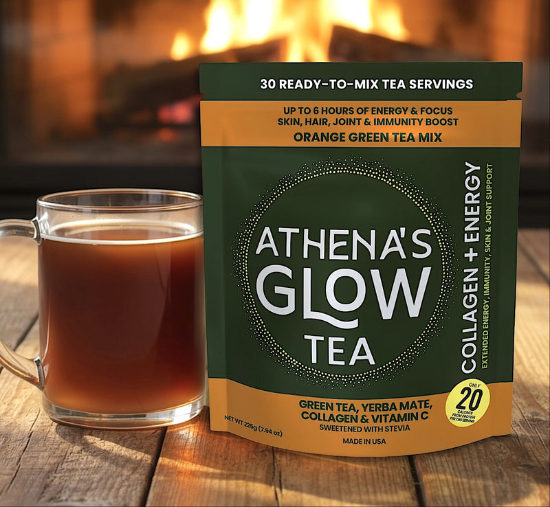 Athena's Glow Tea ORANGE package with a cup of tea on a wooden surface in front of a fireplace.