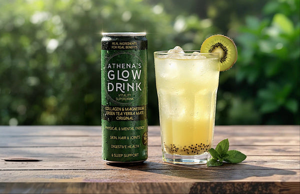 Athena's Glow Drink can and a glass of green juice with a kiwi on a wooden table outdoors.