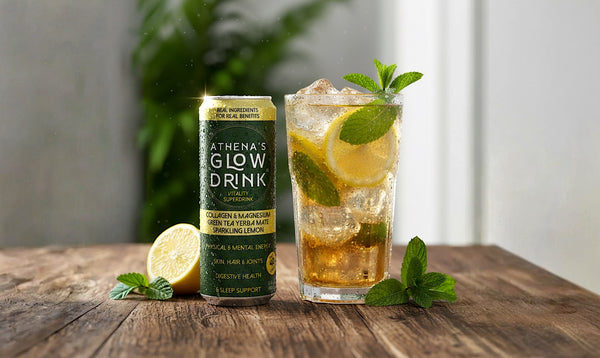 Athena's Glow Drink can next to a glass of a mocktail with ice and mint on a wooden surface.