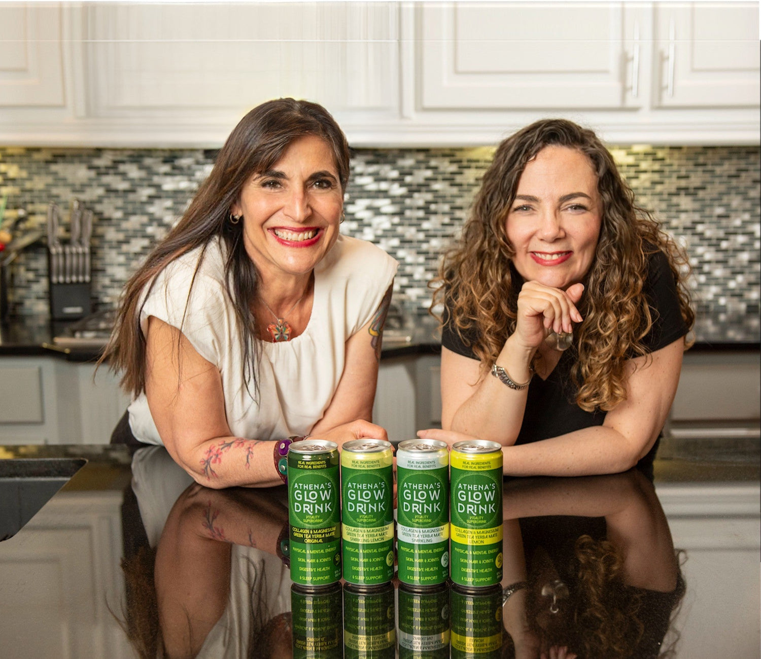 Athena's Glow co-founders sitting at a kitchen counter with cans of Athena's Glow Drinks