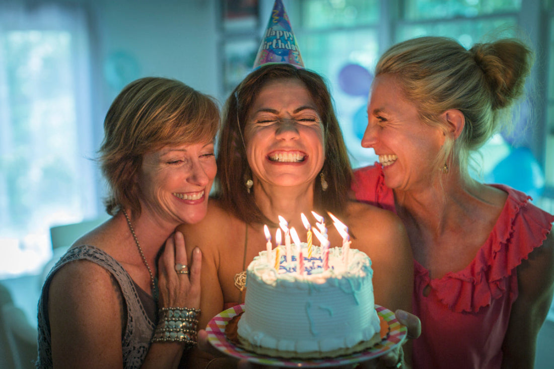 Three women celebrating a birthday with a cake and lit candles.