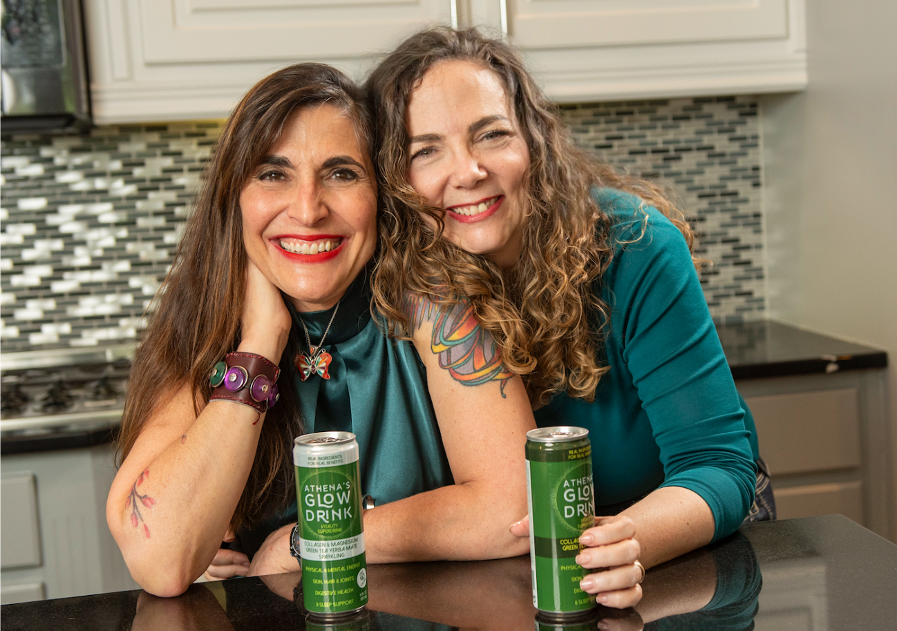 Athena's Glow Drink founders sitting in a kitchen with cans on the counter.