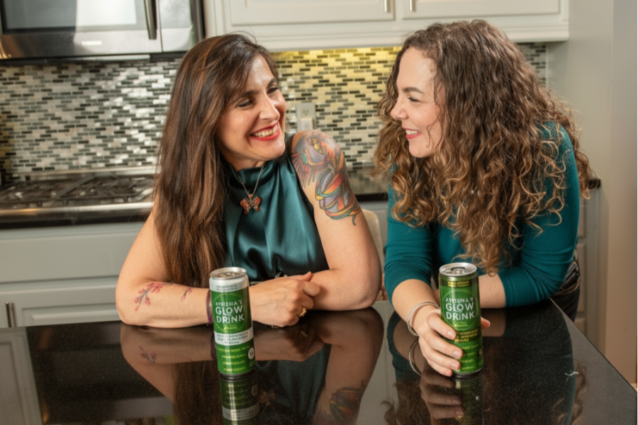 Athena's Glow founders sitting at a kitchen counter with cans of 'Glow Drink'.