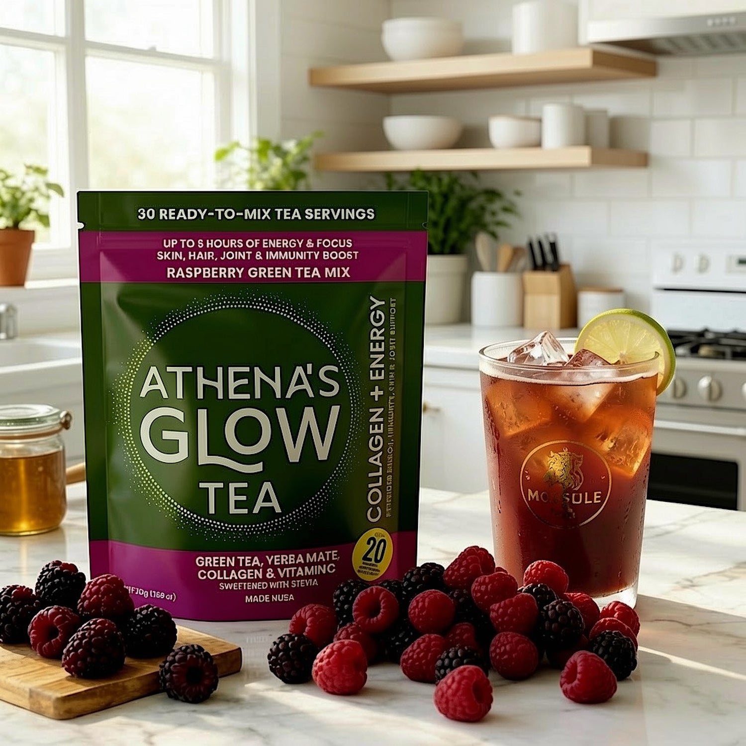 Athena's Glow Tea package with a glass of iced mocktail and fresh berries on a kitchen counter.